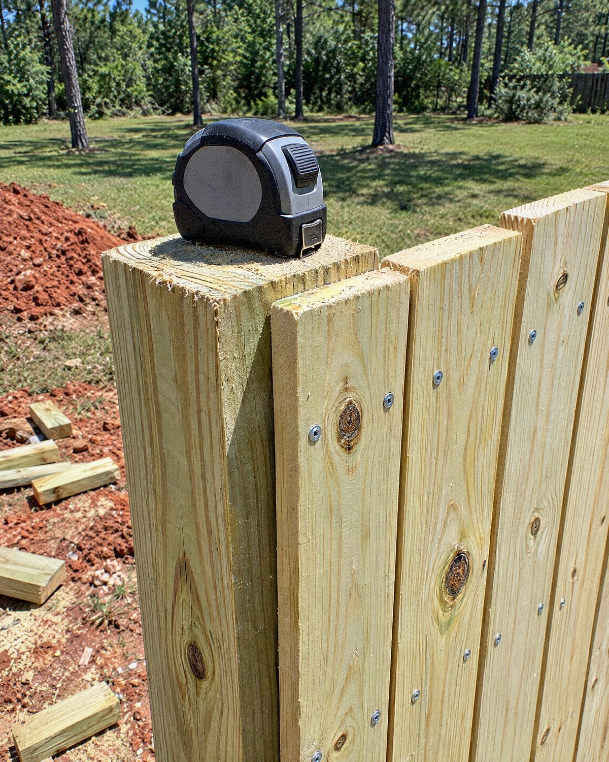 Close-up of a pine fence post and boards with galvanized screws and a tape measure on the post top