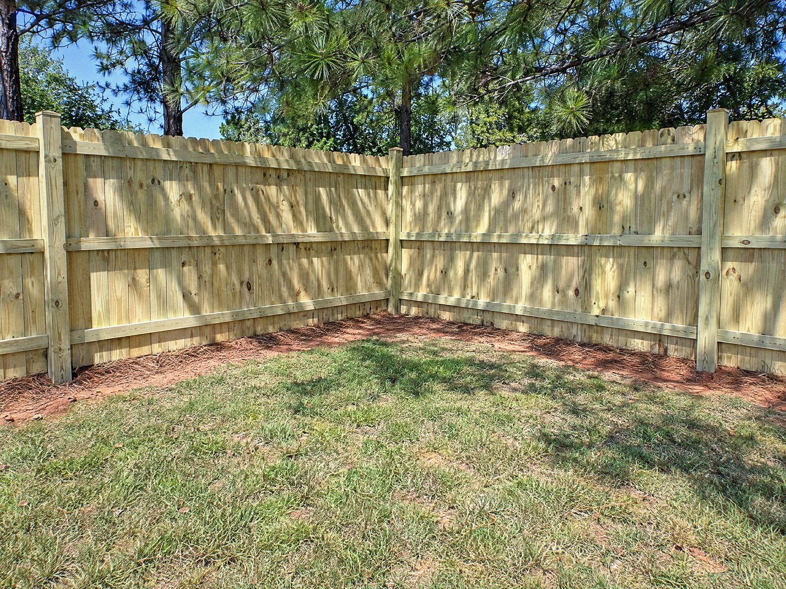 Inside corner of a wood privacy fence seen from the rail side, with posts, rails and pine shade on the boards