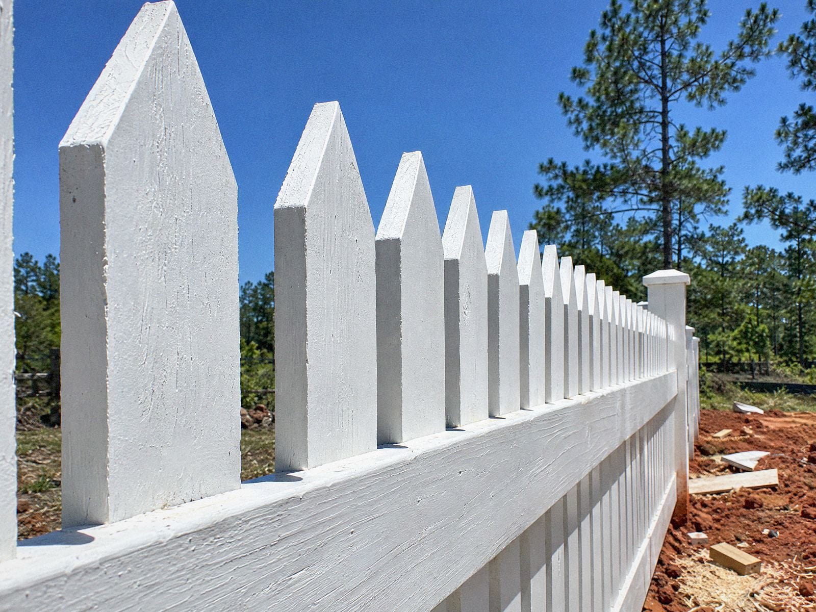 Low-angle close-up of pointed white picket tops against a blue sky