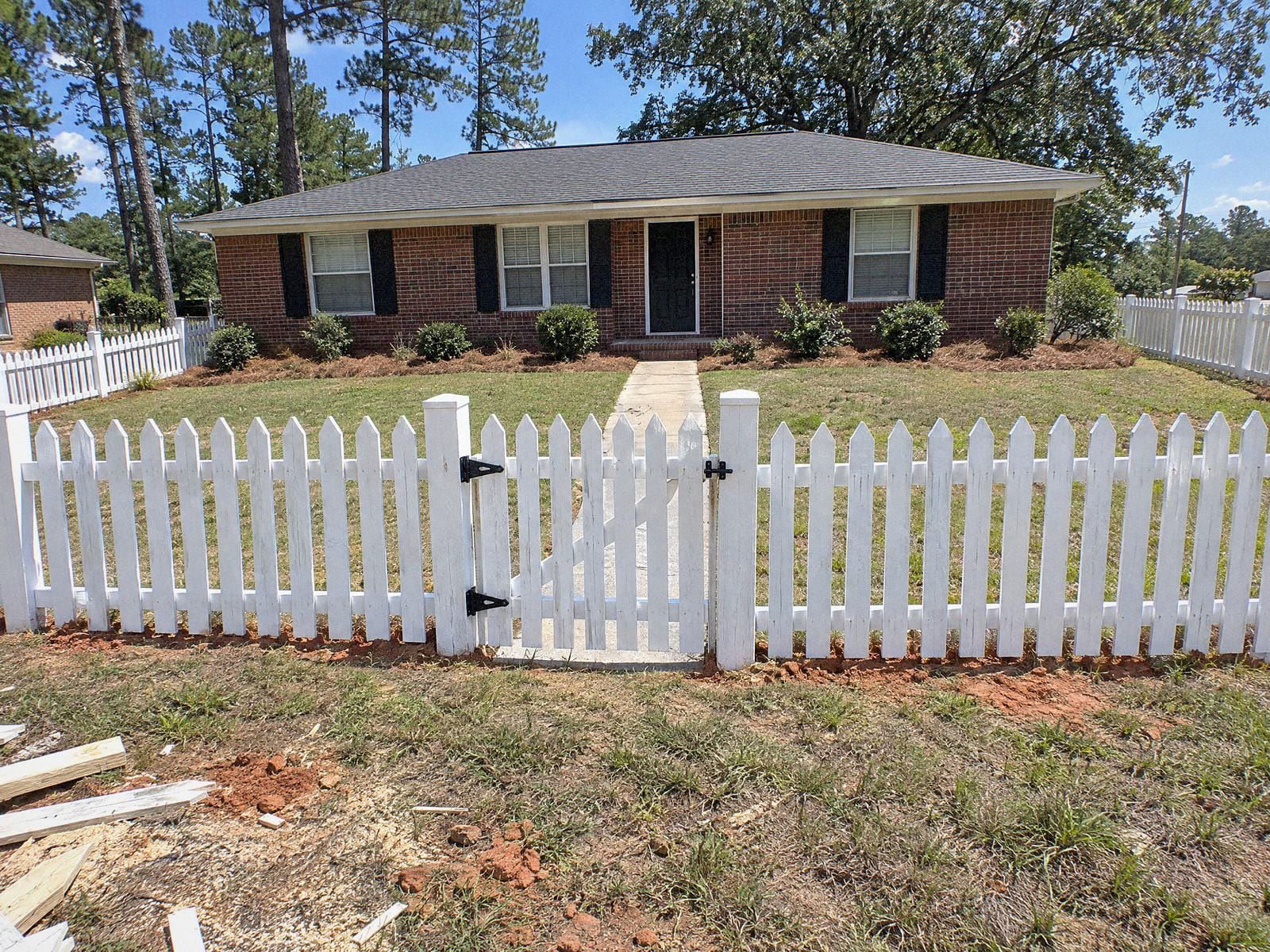 White painted wood picket fence with pointed tops and a walk gate across the front walk of a brick ranch house