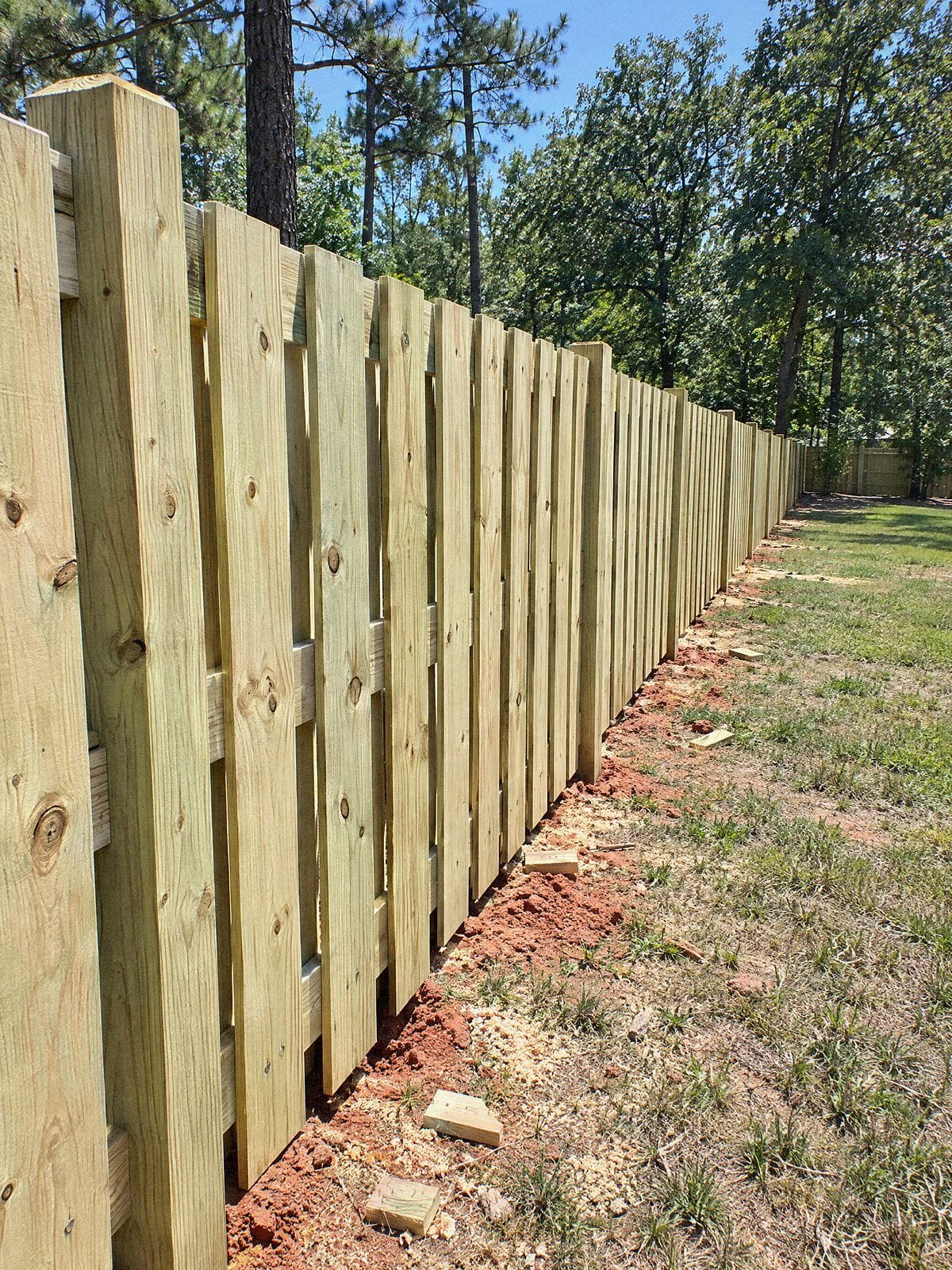 Shadowbox wood fence seen down the line, with boards on both sides of the rails and small gaps between them